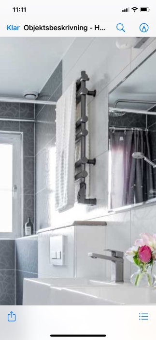 Modernt badrum med gråa kakelväggar, handdukstork, handfat och blomma.