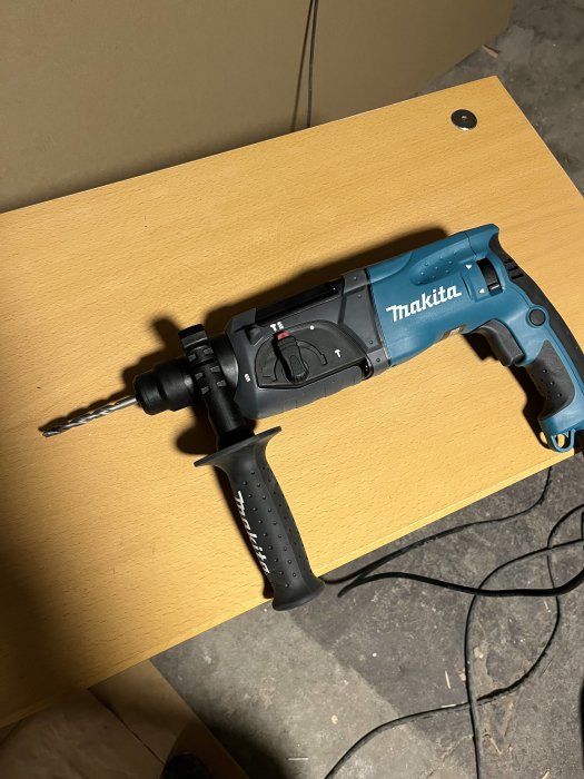 Makita borrmaskin med borr halvt insatt i chucken som ligger på ett brunt bord.