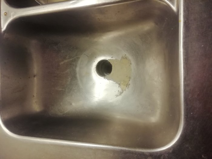 Rostfritt diskho med ett hål runt avloppet där silen ska sitta, tydliga tecken på slitage och användning.