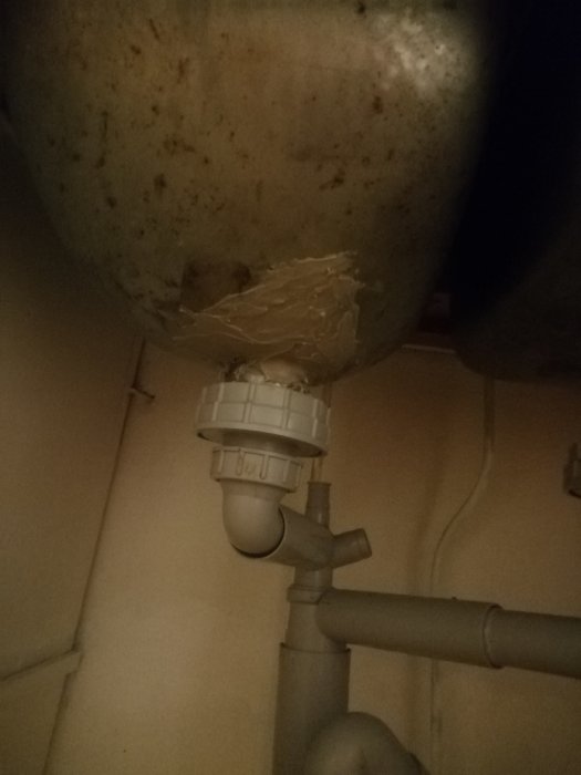 Skadad avloppsstam under handfat med sprickor och skadat material runt avloppsröret.