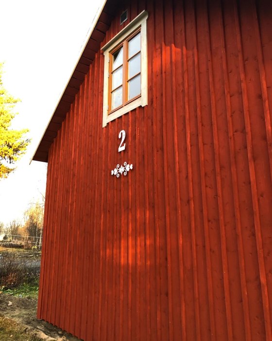 Röd husgavel med ett fönster och dekorativa siffror och blomdekoration.