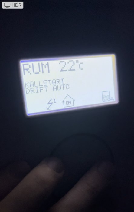 Termostatdisplay som visar rumstemperatur 22°C och texten 'KALLSTART DRIFT AUTO' med symboler för hus och soptunna.