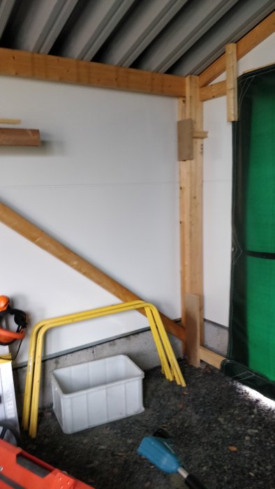 Del av ett garage under renovering med synliga träreglar och isoleringspaneler, verktyg och byggmaterial på golvet.