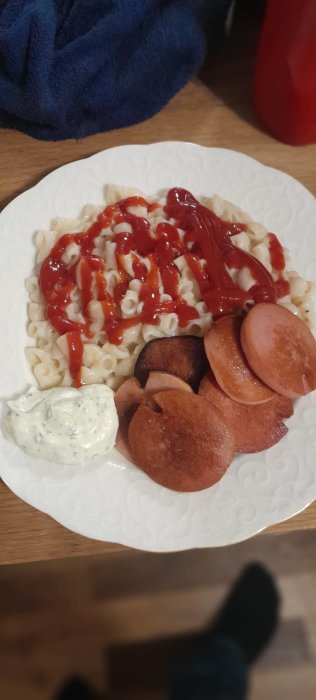 Tallrik med stuvade makaroner och ketchup, stekt falukorv i skivor och en klick remouladsås.