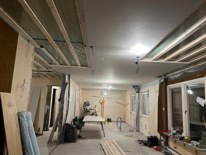 Pågående renovering med gipstak och markerade platser för spottar, omgivet av byggmaterial.
