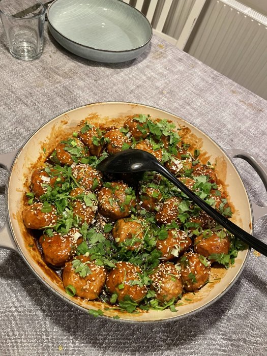 Vietnamesiska köttbullar i sås garnerade med sesamfrön och örter i en stekpanna på ett köksbord.