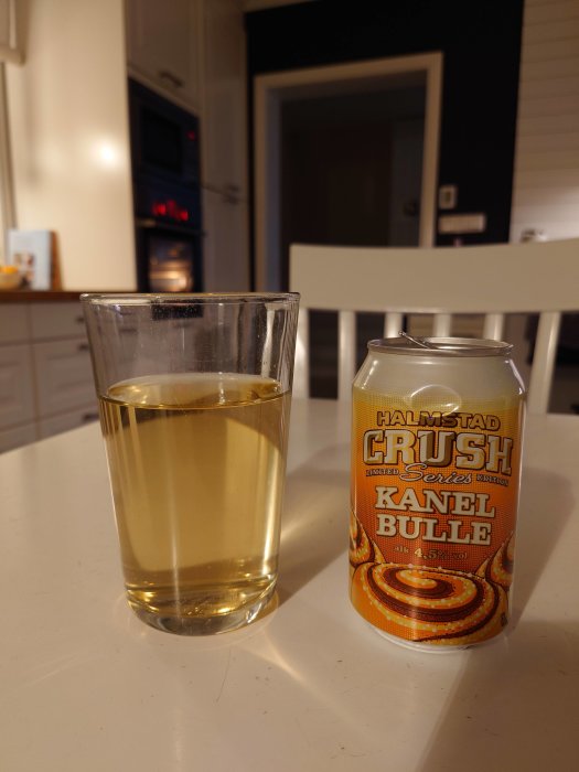 Glas med guldfärgad cider och en ciderburk med texten "Halmstad Crush Kanel Bulle" på ett bord.