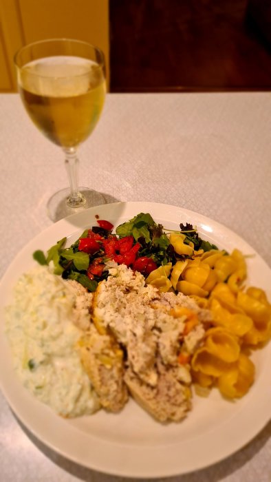 En tallrik med kycklingfärslimpa, fetaost, Västerbottenost, tsatsiki, sallad, pastasnäckor och ett glas Retsina.