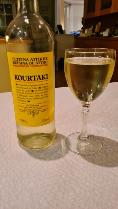 Flaska grekiskt Retsina-vin med märket Kourtaki och ett glas med vin framför.