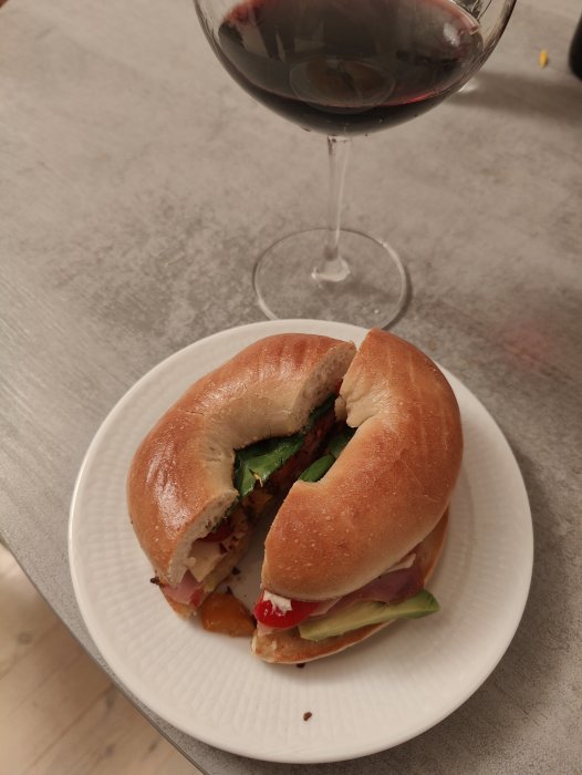 Smörstekt bagel med fyllning på tallrik bredvid ett glas rödvin.