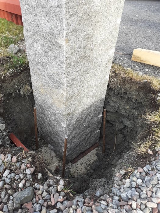Stor granitstolpe på 300 kg placerad i en grävd grop med armeringsjärn som förberedelse för gjutning.