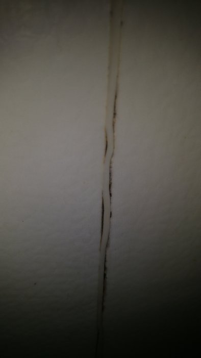 Vertikal spricka i en vit vägg med smutsavlagringar.