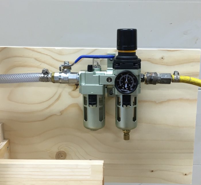 Tryckluftssystem monterat på trävägg med regulator, manometer, ventiler och kopplingar.