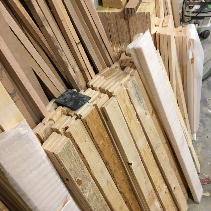 Nyhyvlade trädelar till lådsidor och bakstycken staplade i en verkstad, redo för limning och torkning.