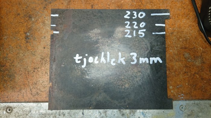 Svart metallplåt med vit text "tjocklek 3mm" och måttmarkeringar på en rostig yta.