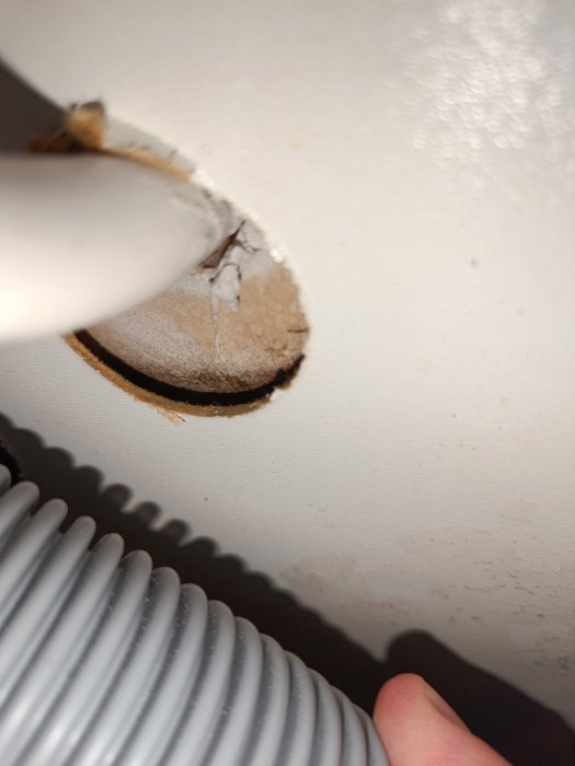 Närbild på ett avloppsrör som går genom ett hål i en vägg, med synliga tecken på slitage runt hålets kanter.