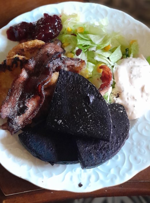 Tallrik med blodpudding, bacon, sallad, lingonsylt och gräddfil.