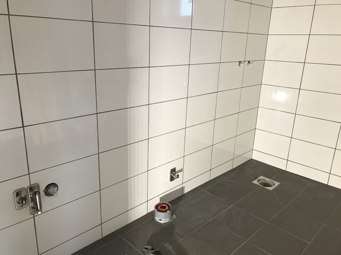 Vägg och golv i badrum med nya kakelplattor och förberedelser för sanitetsinstallationer.