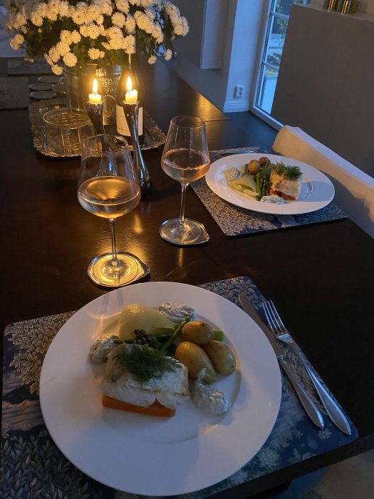 Middagsdukning med torsk, potatis, grönsaker och vitt vin vid levande ljus.