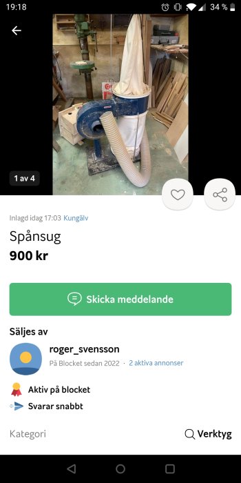 Spånsug i blå och vit med ansluten slang står i en verkstad med trämaterial i bakgrunden.