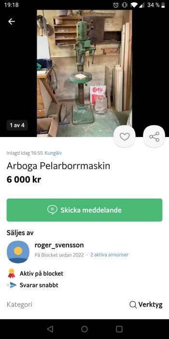 Arboga pelarborrmaskin i arbetsmiljö med borrstativ och hyllor med trädetaljer i bakgrunden.