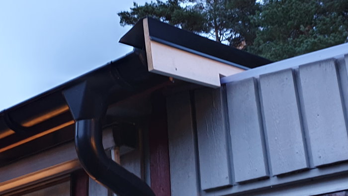 Ränna och stuprör på hus med omlottmonterad vindskiva och träpanel.