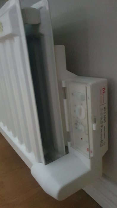 Elektronisk termostat monterad på en radiator med synlig inställningspanel och del av rummet.