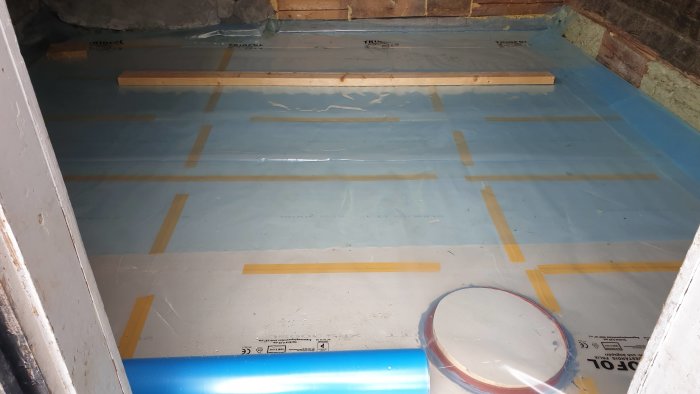 Renoverat golv med cellplastisolering och träreglar på uthusets betongunderlag.