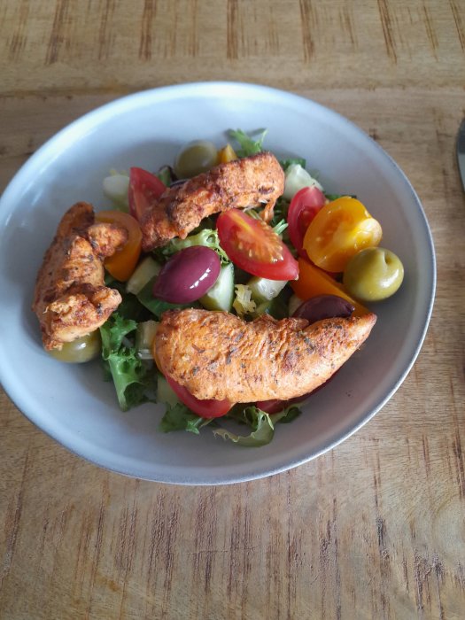 Färsk blandad sallad med kyckling, tomater, oliver och grönsaker serverad i vit skål.