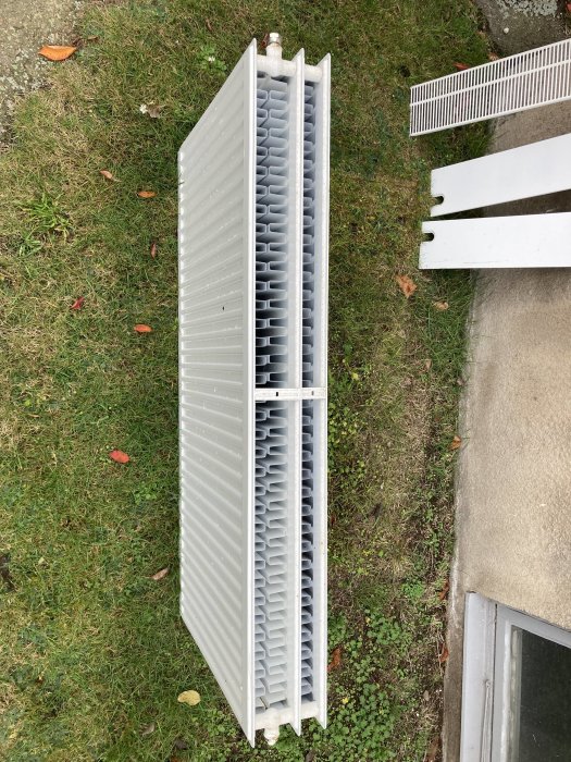 Element för uppvärmning liggandes på gräsmattan vid sidan av vitmålade träplankor.