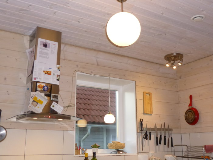 Kök med vit inredning, rostfri fläkt och horisontella träpaneler på taket.
