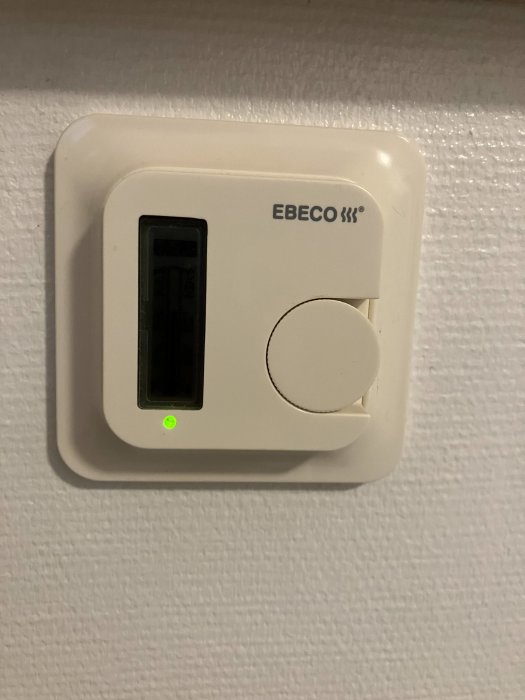 EBECO termostat med digital display och grön lysdiod monterad på vit vägg.