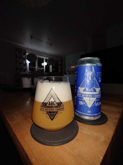 En grumlig öl i ett glas märkt "ABC Apex Brewing Company" och en obruten ölburk med liknande märke på en mörk yta.