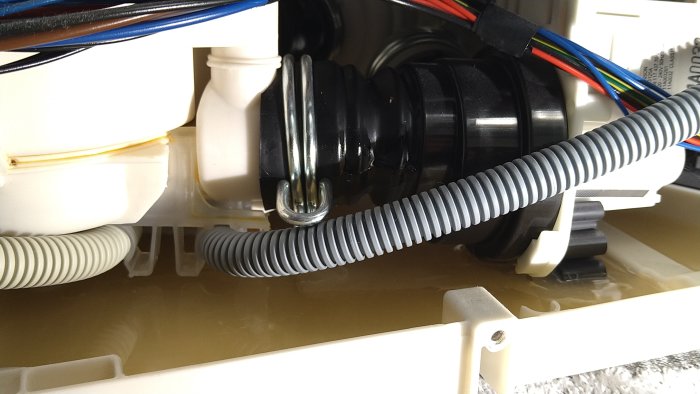 Öppet tråg med vattenläckage och maskindelar, inklusive en frigolitflottör och en svart slang med fuktiga fläckar.