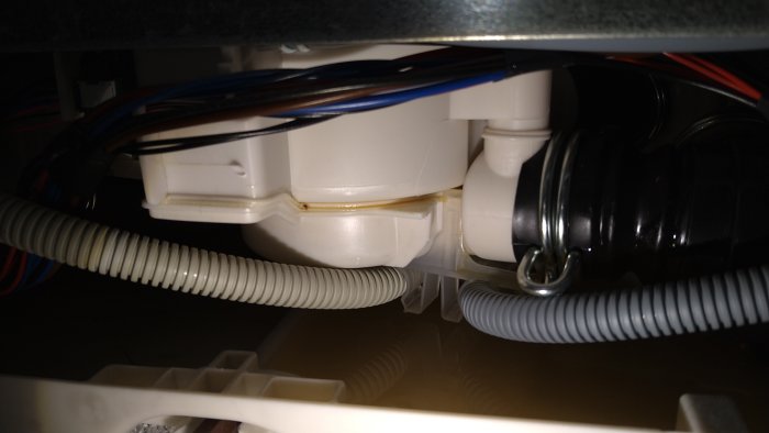 Läckage och fukt längs den vita konstruktionen och slangar under en diskho, med synlig gulaktig substans på skarven.