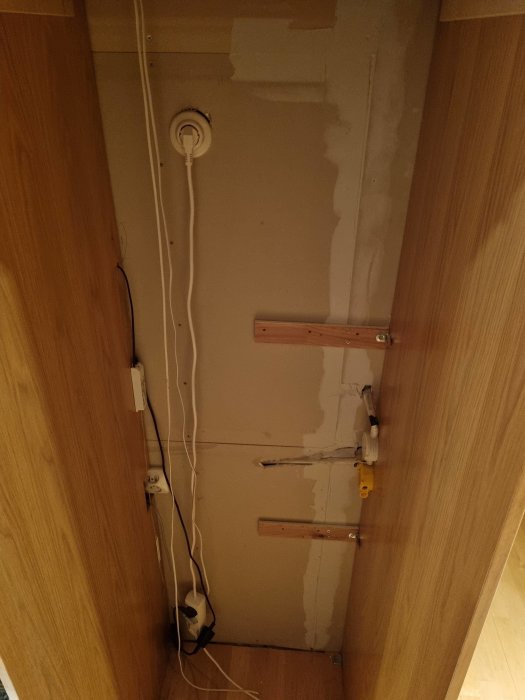 Oorganiserad elkabeldragning på en ofärdig vägg bakom ett kylskåp i en renovering.