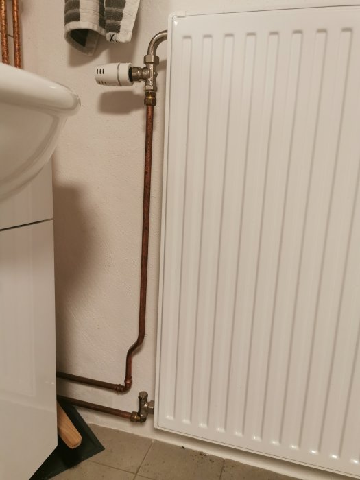 Radiator med termostatventil kopplad till kopparledningar vid en vit vägg.