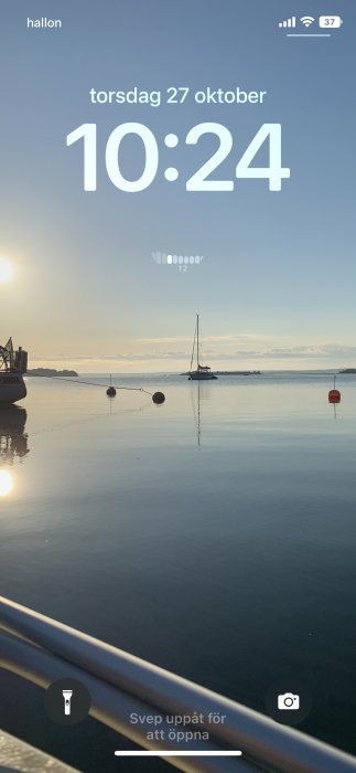 Smartphone skärmdump som visar låst skärm med tid och liten widget, med utsikt över lugnt hav och segelbåt.