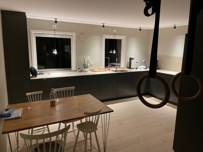 Nytt modernt kök med mörka skåp och vita väggar, träbord och stolar, samt köksö med diskbänk.