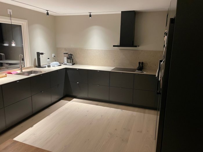Nytt modernt kök med mörka skåp, ljus bänkskiva och trägolv, väntar på ytterligare inredning.