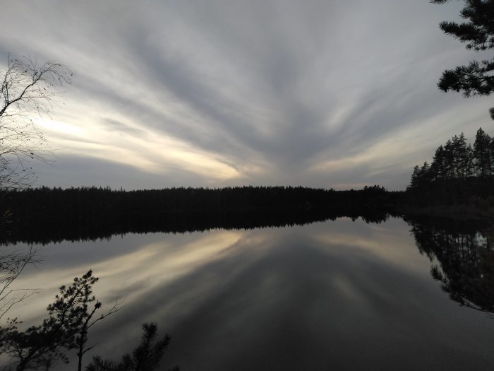 Spektakulära molnformationer reflekterade i en skogssjö vid skymningen.