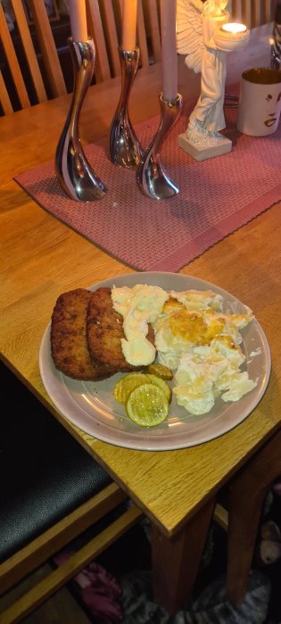 Schnitzel med potatisgratäng, skivad gurka och bearnaisesås på en tallrik på ett hemtrevligt köksbord.