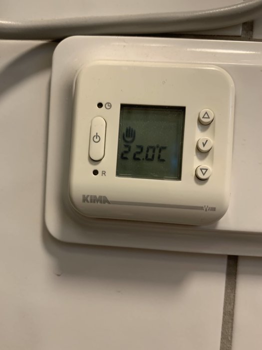 Digital termostat visar inomhustemperatur på 22.0 grader Celsius på en vit vägg.