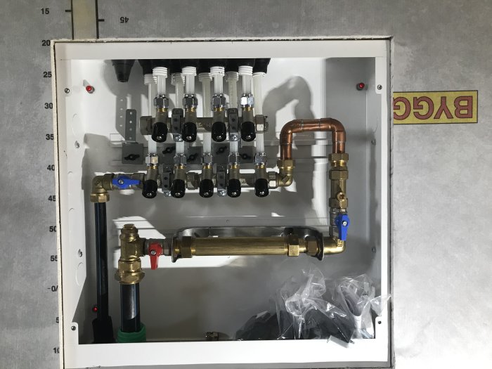 Installerat värmesystem i fritidshus med flera ventiler och kopparledningar i en vit väggmonterad låda.