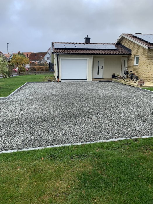 En infart med gårdsgrus framför ett hus med vit garageport och solpaneler på taket.