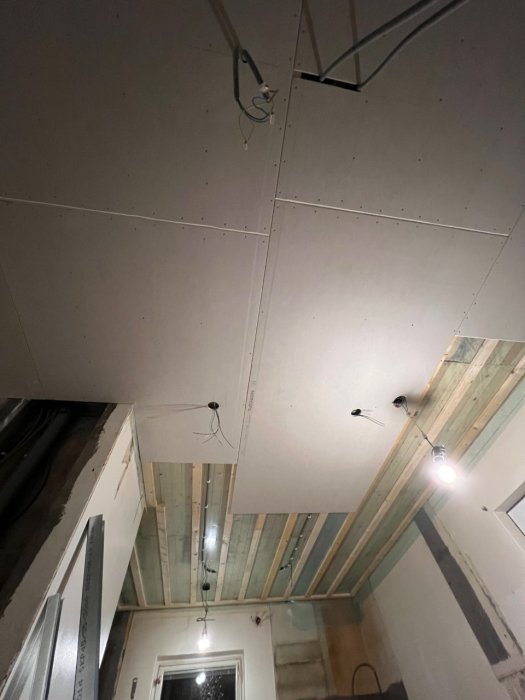 Delvis färdigställt undertak i rum under konstruktion med synliga gipsskivor, träreglar och elinstallationer.