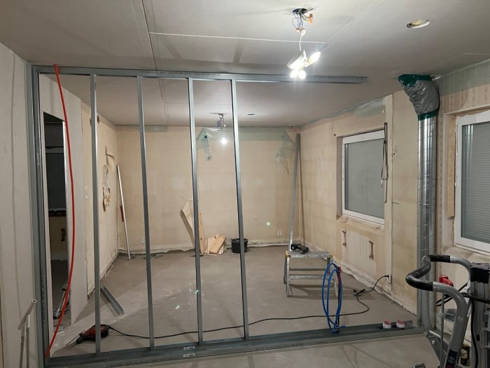 Renoveringsprojekt med pågående installation av metallstomme för väggar i ett rum med synlig isolering och verktyg.