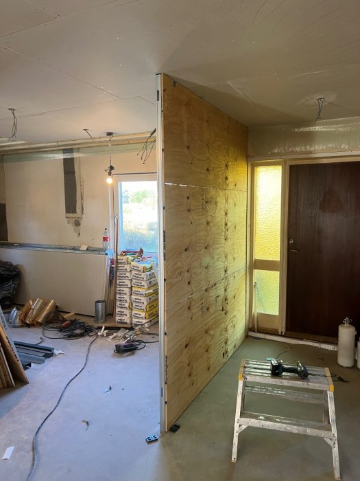En delvis renoverad köksvägg med öppna elinstallationer och en träpanelvägg i ett bygge.
