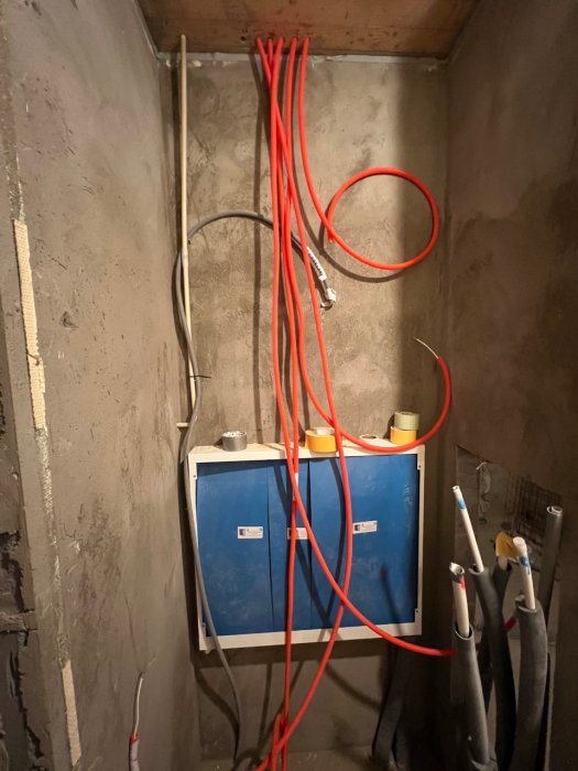 Dragning av röda el- och signal kablar i en ofärdig köksvägg med exponerade grå installationsrör och två blå elcentraler.