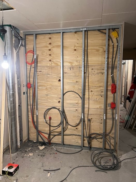 Kabeldragning i en öppen köksvägg med trästomme, oskadade el- och patchkablar samt verktyg och byggmaterial på golvet.